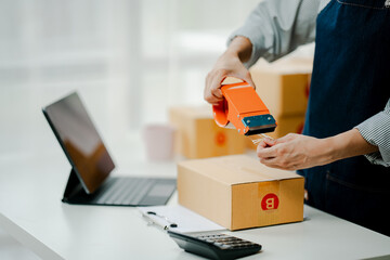 Small online business owner smiling The seller is checking the parcel and packing the product before sending. Preparing packages for SME e-commerce delivery service concepts