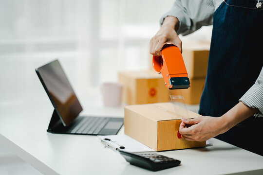 Small online business owner smiling The seller is checking the parcel and packing the product before sending. Preparing packages for SME e-commerce delivery service concepts