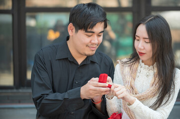 Asian man makes surprise proposal of marriage to girlfriend, Romantic male proposing to woman with wedding ring enjoying surprise engagement together