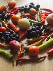 Vertical Close Up of Blue Grapes, Tomatoes, Apples and Colorful Chili Peppers on Wooden Table
