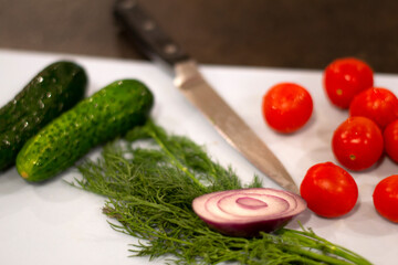 Fresh vegetables for salad cucumber tomatoes onion and dill with knife on the cutting board
