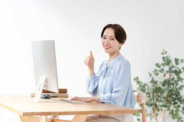 パソコンの前でサムズアップをする女性