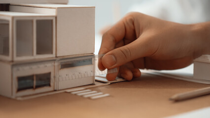 Closeup image of skilled professional engineer hand using ruler measures house model on table with...