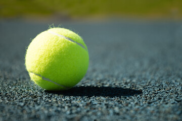 Yellow tennis ball with sunny shadow on blue tennis court with artificial covering. Summer sports. Close up. Copy space.