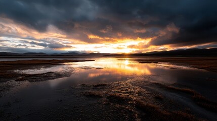 Fototapeta premium A large expanse of water with a cloud-filled sky and a sun sinking behind distant mountains