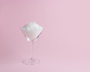 Snow in martini glass on pastel pink background. Minimal Christmas or New Year concept.