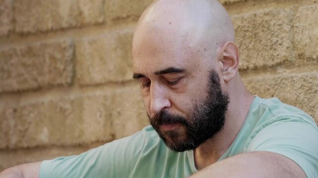 A close-up of a bald man in a green shirt looking sad and thoughtful. His expression shows deep reflection and sadness