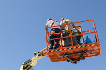 Low angle view of a Two workers on a cherry picker with safety equipment on a sunny day. Copy space