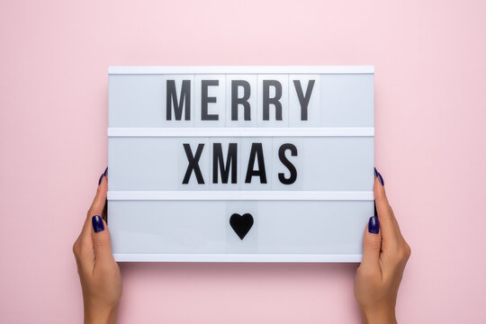 Lightbox with the text MERRY XMAS in women's hands on a pink background. Minimal Christmas or New Year concept.