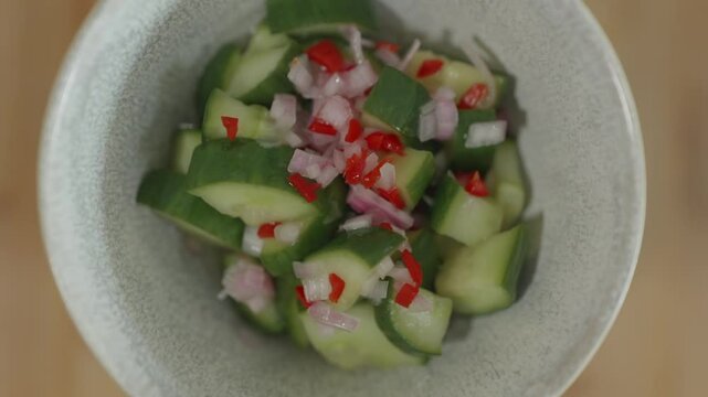 Une salade de pickles de concombre d'&eacute;chalottes d'&eacute;chalottes coup&eacute;s en petits morceaux dans un pot en c&eacute;ramique grise qui tourne vers la droite sur un fond de planche &agrave; d&eacute;couper en bois