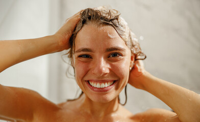 A joyful young woman in the shower, lathering her hair with shampoo, radiating happiness and...