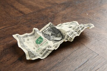 One crumpled dollar banknote on wooden table, closeup