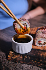 Savoring delicious sushi roll dipped in sauce at a cozy restaurant in the evening with friends