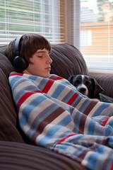 teenager sleeps next to his pet covered with a colorful shredded blanket with headphones on the sofa at home, vertical, peace, relaxation, tranquility, best friend,
