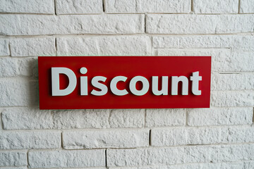 Naklejka premium Bright discount sign on a white brick wall, emphasizing savings and promotions for shoppers in retail environments.
