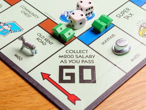 Close up of playing pieces passing Go square and being paid a salary on a UK London Monopoly board game