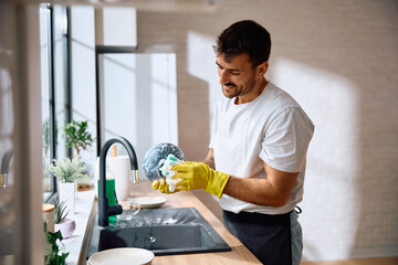 Smiling man washing dishes in kitchen.