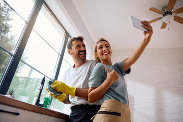 Obraz premium Happy woman taking selfie with her boyfriend who is doing the dishes in kitchen.