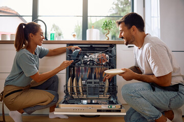 Young happy couple using dishwasher in  kitchen.