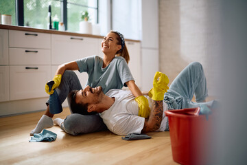 Young happy couple relaxing on  floor after cleaning their house together.