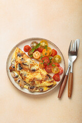 Mushroom omelette with cherry tomato salad on the side, served on a plate. Healthy breakfast or lunch top view