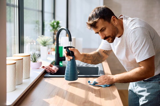 Young man wiping kitchen counter while cleaning house.