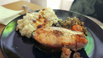Grilled salmon steak served with creamy mashed potatoes and a side of sautéed lentils with carrots, showcasing a balanced and nutritious meal presentation