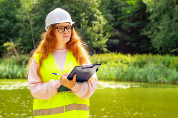 Female ecologist with a tablet writes down technical data of a lake water analysis in a forest. Forestry inspector.