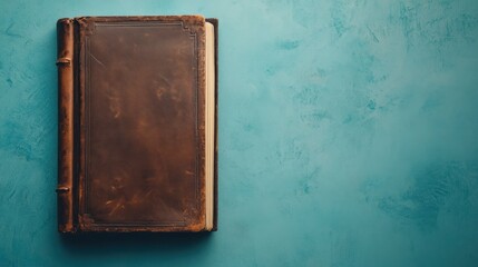 A vintage leather-bound book rests on a textured blue surface, suggesting a sense of history.
