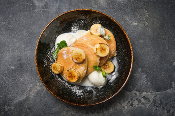 delicious serving of soft pancakes topped with banana slices and a scoop of vanilla ice cream, presented in a textured bowl.