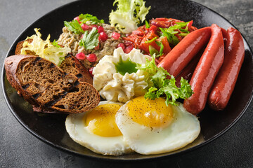 hearty breakfast featuring sunny side up eggs, grilled sausages, tomatoes, salads, and bread slices on a dark plate.