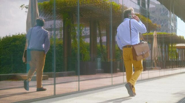 Multi sequence shots of elderly contented businessman walking by glass building in urban city and talking on phone