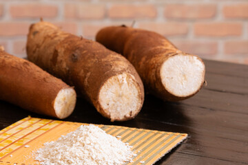 A portion of cassava flour on top of a bamboo mat, and cassava roots in the background and out of focus