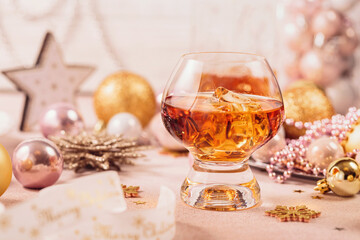 Glass of whiskey or bourbon with festive Christmas decoration on light beige background. New Year, Christmas and winter holidays whiskey mood concept