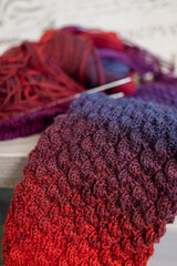Fototapeta premium Knitted items. Self-made warm socks. Knitting pattern. Quality wool thread. Red-blue gradient. Cozy details. Home comfort. Colored yarn. Winter clothes. Christmas gift. Calm winter hobby. Wool socks.
