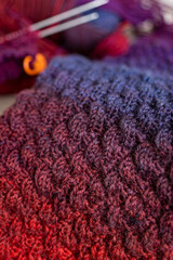 Fototapeta premium Knitted items. Self-made warm socks. Knitting pattern. Quality wool thread. Red-blue gradient. Cozy details. Home comfort. Colored yarn. Winter clothes. Christmas gift. Calm winter hobby. Wool socks.