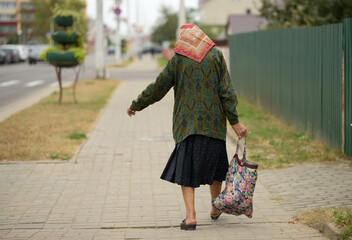 an elderly woman in a headscarf carries a heavy bag