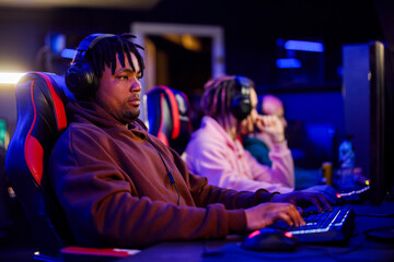 Multiracial professional gamer guy with headset playing games in cybercafe