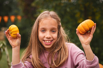 Close up. Portrait of a child girl on Pumpkin farm. 8 years old girl smiles and holds tiny pumpkins.