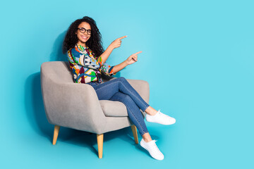 Photo of cheerful cute woman wear stylish clothes sit comfortable armchair presents empty space isolated on blue color background