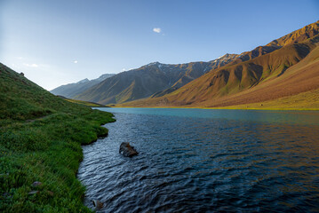 Chandratal lake, Moon Lake during Sunset with crystal clear water in between mountains surrounded by snowcapped mountains.