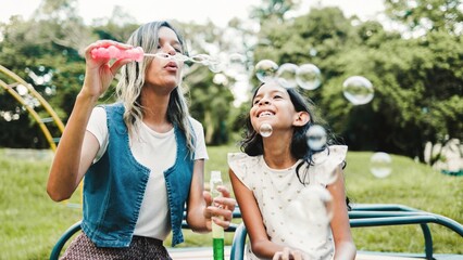 Family, Happy hispanic mother and daughter play blowing soap bubbles at park city. Latin mom having fun with child