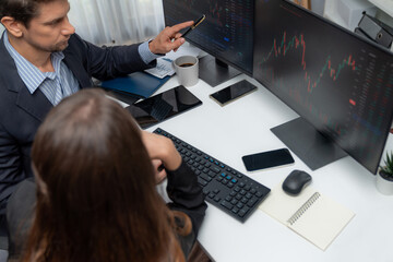 Two business traders discussing on dynamic stock market in currency rate investment trading on two pc screens with compare real time graph on risk or profit point of data at modern office. Postulate.