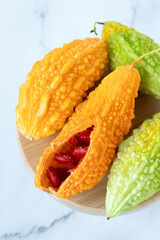 Ripe karela (bitter melon, Momordica charantia) with orange and green color isolated on white marble background. Close-up. Top table view. Organic fresh tropical fruit.