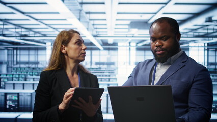 Teamworking technicians managing data center with advanced technology using devices. Coworkers in...