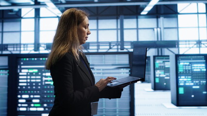 Woman walking in high tech facility, using laptop to patch network issues leading to slow data transfer rates. Employee in data center fixing errors affecting servers performance, camera A