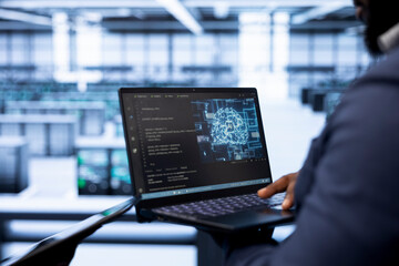 System administrator in data center using laptop to visualize artificial intelligence neural...