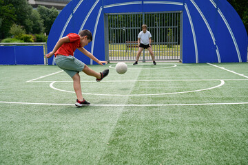 Young boy scoring a soccer goal with his mother as the goalkeeper, enjoying a sunny game.