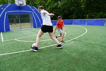 Fototapeta premium Mother teaches son soccer skills while playing together on a green field under the sun