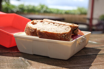Packed in lunch sandwich in tupperware on picnic table. Wholegrain bread and cheese with apple slice. Pack out, pack in garbage and bring your food on hikes and to trekking. Selective focus.